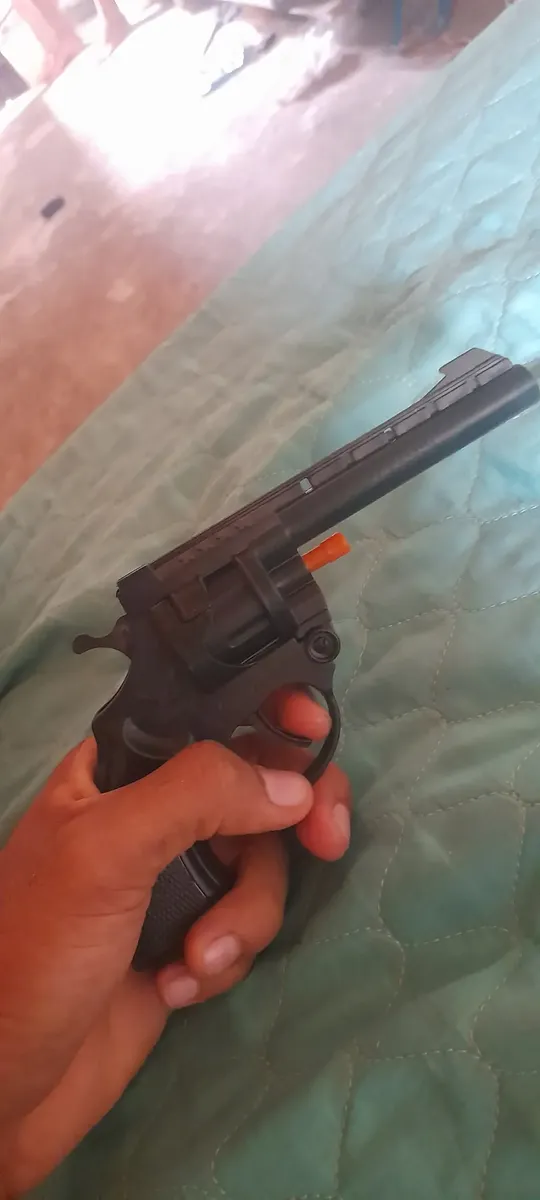 Cliente segurando o revólver de brinquedo preto com ponta laranja.