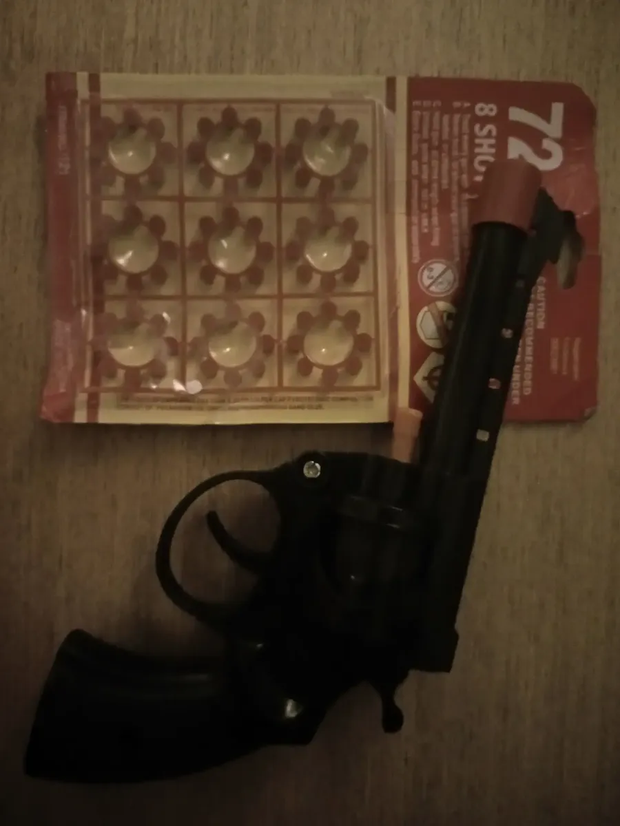 Revólver de brinquedo apoiado ao lado da cartela de espoletas de 72 tiros.